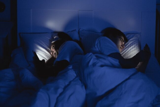 Couple lying in bed on phones